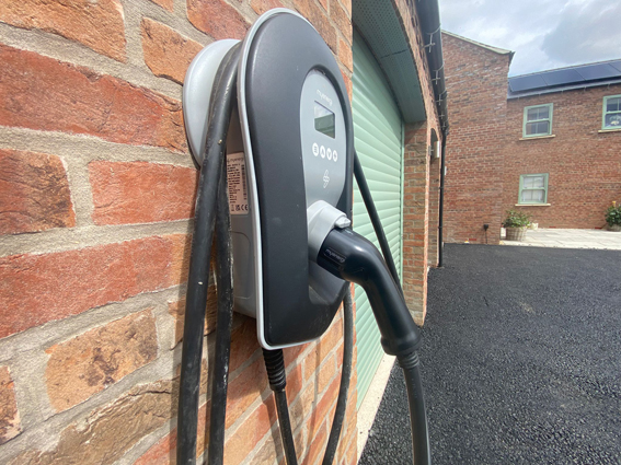 A Zappi Electric Car Charger mounted on the wall of a double garage with green doors
